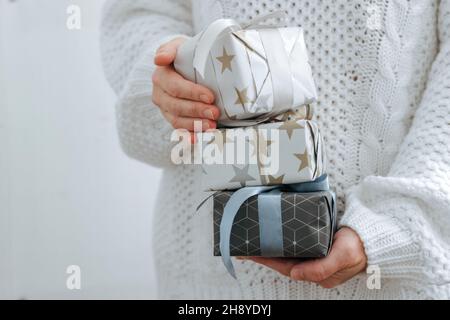 Ein Mädchen in weißem Pullover hält Weihnachtsgeschenke. Weibliche Hände halten Weihnachtsboxen. Das Konzept der Urlaubsvorbereitung Stockfoto