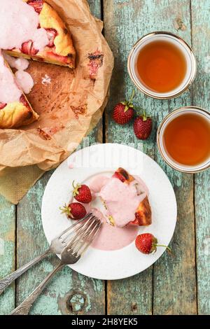 Leckere hausgemachte Kuchen mit Erdbeeren und Sahnesauce serviert mit schwarzem Tee vertikal Stockfoto