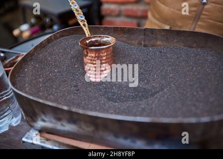 Aromatischer Kaffee, der in heißem Sand gebrüht wird - türkischer Kaffee, der in Cezve braut Stockfoto