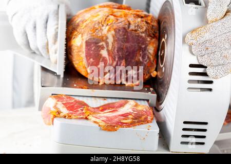 Nahaufnahme eines isolierten Bildes, das einen Metzger oder Koch zeigt, der einen großen gefrorenen, ausgehärteten Fleischblock auftrennt. Türkische Pastirma, Pastrami, Schinken, Rindfleisch-Konzept. Die Person w Stockfoto