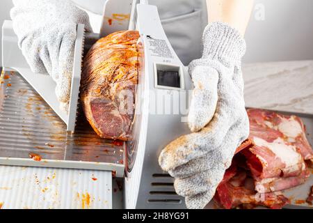 Nahaufnahme eines isolierten Bildes, das einen Metzger oder Koch zeigt, der einen großen gefrorenen, ausgehärteten Fleischblock auftrennt. Türkische Pastirma, Pastrami, Schinken, Rindfleisch-Konzept. Die Person w Stockfoto