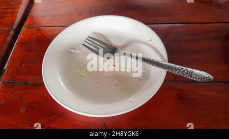 Der Teller, der vom Verzehr des Kuchens übrig blieb, hatte ein Stück Kuchen auf den Teller geklebt und eine Gabel wurde vor dem Waschen auf den Teller gelegt. Stockfoto