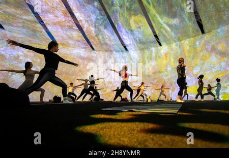 Toronto, Kanada. 2nd Dez 2021. Am 2. Dezember 2021 nehmen Menschen an einem Yoga-Kurs während der Ausstellung „Beyond Monet“ im Metro Toronto Convention Center in Toronto, Kanada, Teil. Durch das immersive Kunsterlebnis während der Ausstellung bietet der wöchentliche Yoga-Kurs unterschiedliche Erfahrungen für alle Altersgruppen und Niveaus. Quelle: Zou Zheng/Xinhua/Alamy Live News Stockfoto