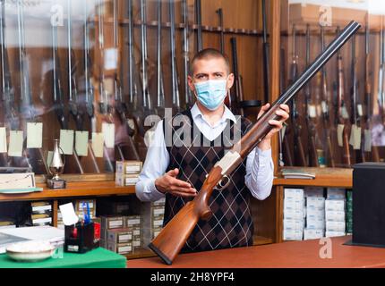 Verkäufer in Schutzmaske zeigt einen Kampf winchester im Waffenladen Stockfoto