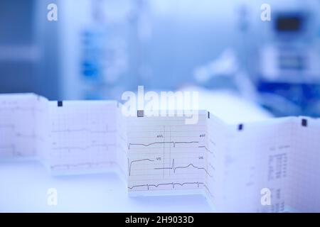 EKG-Diagramm auf dem Tisch der Krankenschwester auf dem Hintergrund des Patienten, der in seinem Bett liegt, gefaltet. Stockfoto