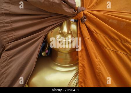 Buddha-Statue in einer Fabrik für buddhistische Objekte in Bamrung Muang Rd., Bangkok, Thailand, ein Auge, das hinter einem orangefarbenen und braunen Stoffbezug herausgucken kann Stockfoto