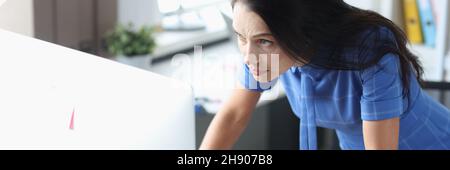 Seriöse Frau, die vor dem Computer steht und auf den Monitor schaut Stockfoto