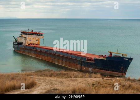 Surow-ein großes altes Schiff, das an der russischen Küste zerstört und am Strand verlassen wurde. Auf der Wasseroberfläche sind Spuren von Ölprodukten zu sehen Stockfoto