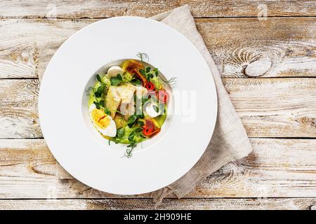 Gourmet-Fischsalat. Kabeljaufilet, Gemüse, Avocado-Pastete und frische Kräuter. Restaurant serviert. Das Gericht des Küchenchefs. Gesundes und leckeres Essen auf einem hölzernen Backgrou Stockfoto