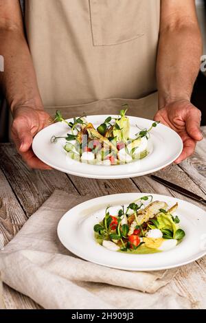 Weibliche Hände halten einen Gourmet-Fischsalat. Pangasius-Dori-Filet, Gemüse, Avocado-Pastete, Mozzarella und frische Kräuter. Restaurant serviert. Chefkoch Stockfoto