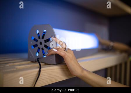 Das Mädchen schaltet die ultraviolette Lampe im Zimmer ein. Stockfoto