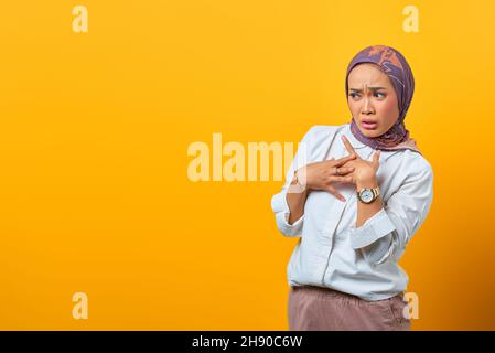 Schockierte asiatische Frau mit der Hand in der Brust und Blick auf leeren Raum über gelben Hintergrund Stockfoto