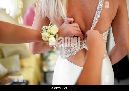 Rückansicht der Ernte unkenntlich Brautjungfer knöpfend bis elegantes Kleid der anonymen Braut mit langen blonden Haaren vor der Hochzeitszeremonie Stockfoto