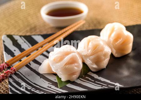 Von oben von leckeren Garnelen Dim Sum serviert auf Keramikplatte mit Essstäbchen in der Nähe Schüssel mit Soja auf den Tisch gelegt Stockfoto