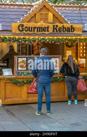 Mann und Frau stehen an einem Kebab-Fastfood-Stand auf einem weihnachtsmarkt, Gourmet-Kebabs zum Mitnehmen, Kebabs und heiße Lebensmittel-Marktstands Schlange Stockfoto