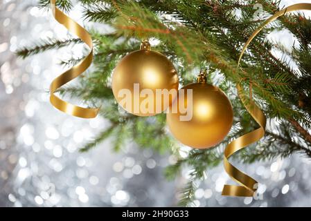 Weihnachtsschmuck. Zwei goldene Kugeln und Serpentinen locken auf einem Zweig eines weihnachtsbaums auf einem silbernen Bokeh-Hintergrund Stockfoto