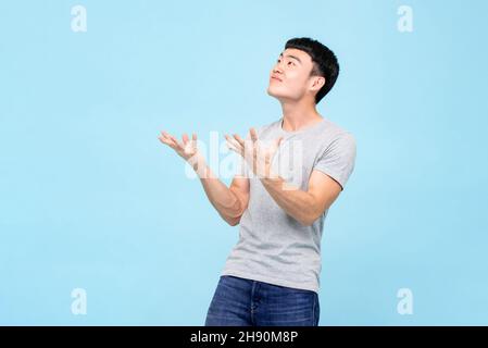 Asiatischer Mann, der mit einem schockierten Gesicht die Hände aufhob und auf einem hellblauen Hintergrund auf leeren Raum über dem Studio schaute Stockfoto