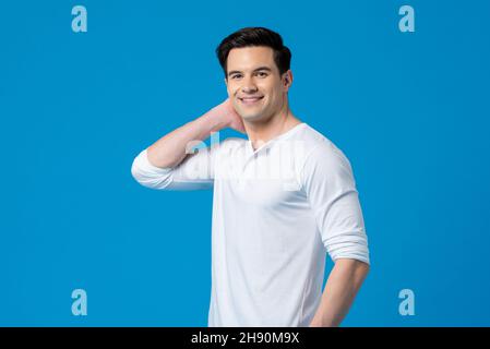 Waist-up-Aufnahme von lächelndem glücklichen jungen, hübschen kaukasischen Mann in schlichtem weißen T-Shirt, der auf einem isolierten blauen Hintergrund die Kamera anschaut Stockfoto