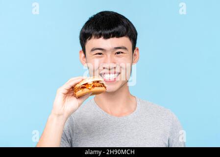 Junger asiatischer Mann sucht Hamburger in hellblau isoliert Hintergrund Stockfoto