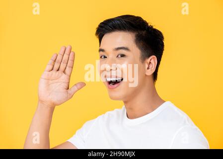 Junger hübscher asiatischer Mann winkt Hand und sagt hallo im isolierten gelben Studiohintergrund Stockfoto