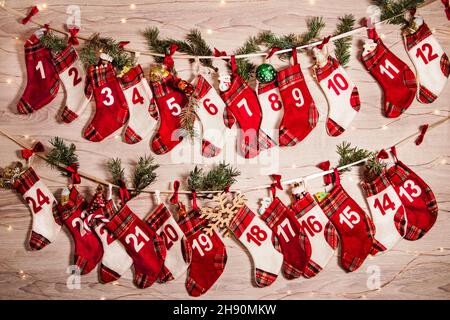 Adventskalender mit Geschenken in Kindersocken, Zweigen eines Weihnachtsbaums, Girlandenlichtern auf einem hölzernen Hintergrund. 24 Socken des Adventskalendes Stockfoto