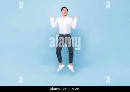 Junger asiatischer Mann, der mit offenen Handflächen springt und auf einem isolierten hellblauen Hintergrund aufschaut Stockfoto