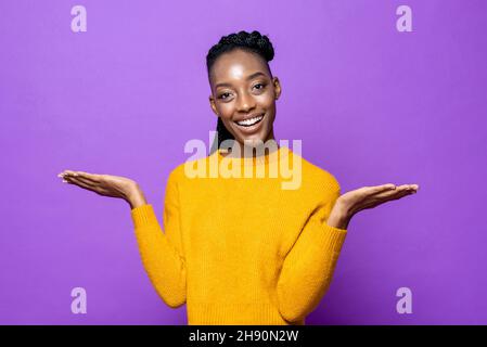 Lächelnde junge afroamerikanische Frau, die die Hände öffnet, um den Raum im isolierten purpurnen Studiohintergrund zu leeren Stockfoto