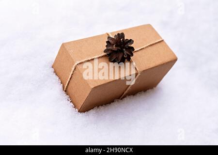 Geschenk in Bastelkiste mit Kieferkegel auf weißem Schnee, umweltfreundliche Öko-Konzept Weihnachten und Neujahr Null Abfall dekoriert Stockfoto