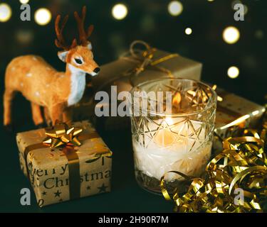 Frohe Weihnachten. Weihnachtskerze mit Rentieren, weihnachtsgeschenken und Weihnachtslichtern auf einem Tisch. Weihnachten Konzept Hintergrund. Selektiver Fokus Stockfoto