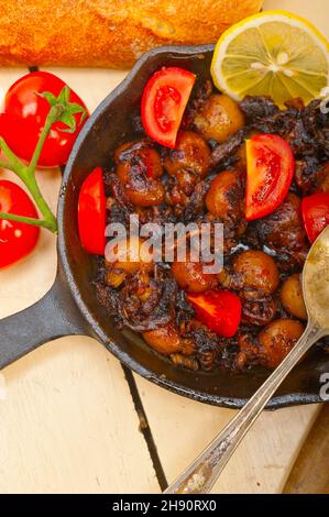 Baby Tintenfisch über rustikalen Holztisch auf eisernen Pfanne mit Tomaten und Zwiebeln gebraten Stockfoto