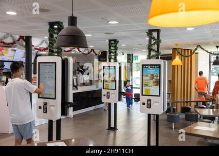 Junger Mann, der mit einem elektronischen Touchscreen Essen bestellt, McDonalds Restaurant Cafe in Sydney, Facemark aufgrund einer covid 19 Pandemie Stockfoto