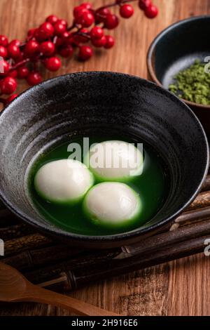 Nahaufnahme des großen Matcha tangyuan (tang Yuan) mit süßer Matcha-Suppe in einer Schüssel auf Holztischhintergrund für Festessen. Stockfoto