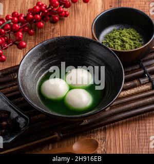 Nahaufnahme des großen Matcha tangyuan (tang Yuan) mit süßer Matcha-Suppe in einer Schüssel auf Holztischhintergrund für Festessen. Stockfoto