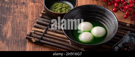 Nahaufnahme des großen Matcha tangyuan (tang Yuan) mit süßer Matcha-Suppe in einer Schüssel auf Holztischhintergrund für Festessen. Stockfoto