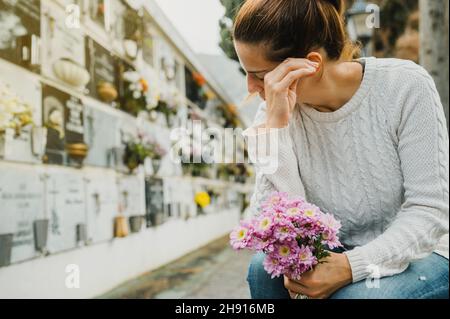 Frau mit Blumen weint in der Nähe der Säulengrube auf dem Friedhof Stockfoto