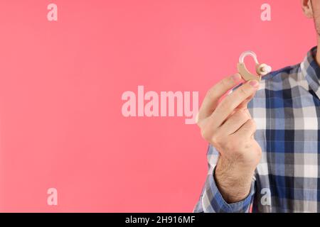 Junger Mann hält Hörgeräte auf rosa Hintergrund Stockfoto