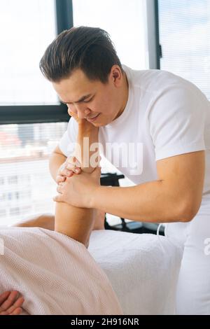 Nahaufnahme eines professionellen männlichen Masseurs mit starken Händen, der nach dem Sport-Training die Wadenmuskulatur am Unterschenkel des Muskelathleten massiert Stockfoto
