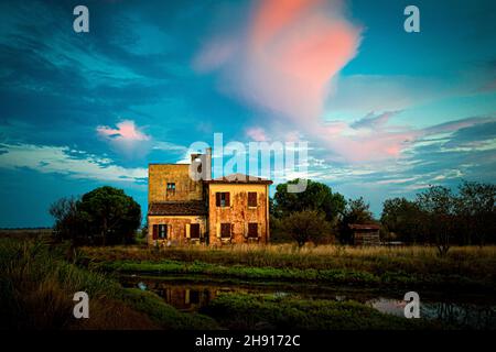 Alte verwitterte verlassene Hütte in den Tälern von Comacchio unter einem blau bewölkten Himmel Stockfoto