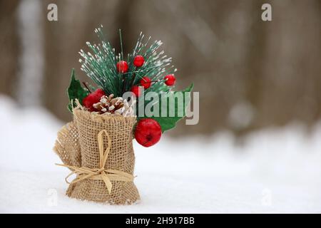 Grußkarte mit Weihnachtsschmuck im Schnee auf Winterwald Hintergrund. Leinenbeutel mit Neujahrsbaum, Tannenzapfen und roten Beeren Stockfoto