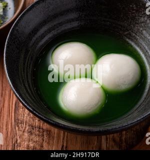 Nahaufnahme des großen Matcha tangyuan (tang Yuan) mit süßer Matcha-Suppe in einer Schüssel auf Holztischhintergrund für Festessen. Stockfoto