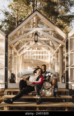 In voller Länge Porträt eines lächelnden Paares, das auf der Hüttentreppe sitzt Stockfoto