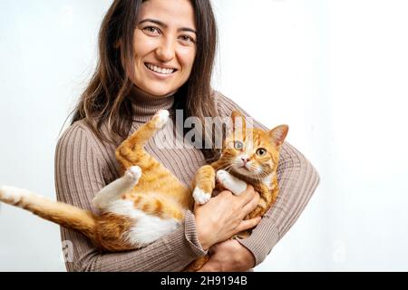 Nahaufnahme der jungen erwachsenen Frau, die mit einer häuslichen Tabby-Katze auf isoliertem Hintergrund lächelt. Konzept für Katzen- und Tierliebhaber. Stockfoto