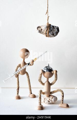 Die Menschen lehnen die Impfung gegen den Corona-Virus ab. Holzmann in Zinnfolienhut, der unter schwerem Stein saß, fürchtete sich, geimpft zu werden. Holzspielzeug Stockfoto