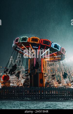 Glühend festliches Karussell, das auf der Straße unter dem fliegenden Schnee wirbelt Stockfoto