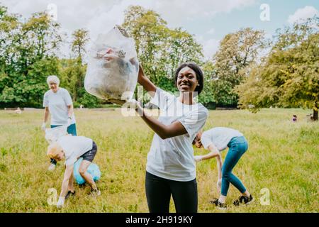 Portrait einer Umweltschützerin, die Plastikmüll zeigt, während Freiwillige im Park putzen Stockfoto