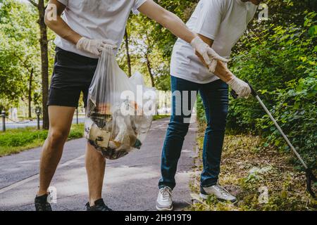 Niedriger Teil von männlichen und weiblichen Freiwilligen, die im Park Plastik aufsammeln Stockfoto