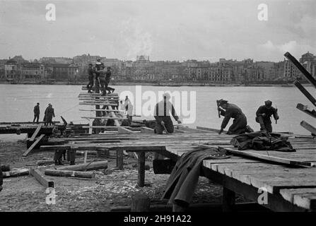 Warszawa, 1947-04. Saperzy z i Warszawskiego Pu³ku Pontonowego buduj¹ prowizoryczny most niskowodny na Wiœle. NZ. Saperzy buduj¹ wjazd na nowy most od strony Pragi. W tle zabudowania Powiœla. wb PAP Dok³adny dzieñ wydarzenia nieustalony. Warschau, April 1947. Die Sapper des Warschauer Pontoon-Regiments von 1st bauen eine provisorische Niedrigwasserbrücke an der Weichsel. Im Bild: Sappers Nagelbalken am Eingang zur Brücke vom Ufer des Praga Distrikts. Im Hintergrund Gebäude des Bezirks Powisle. wb PAP Stockfoto