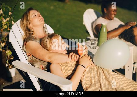 Mutter entspannt sich mit Tochter im Hinterhof auf dem Liegestuhl während des sonnigen Tages Stockfoto