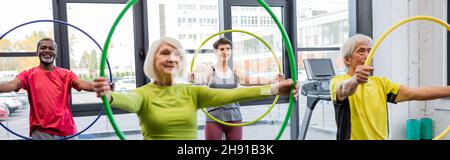 Lächelnde multikulturelle Menschen trainieren mit Hula Hoop Reifen im Fitnessstudio, Banner Stockfoto