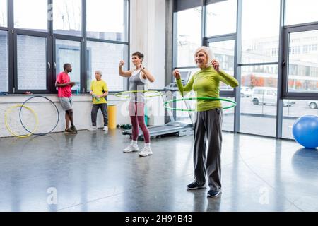 Glückliche ältere Frau, die mit dem Hula Hoop Reifen im Sportzentrum trainiert Stockfoto